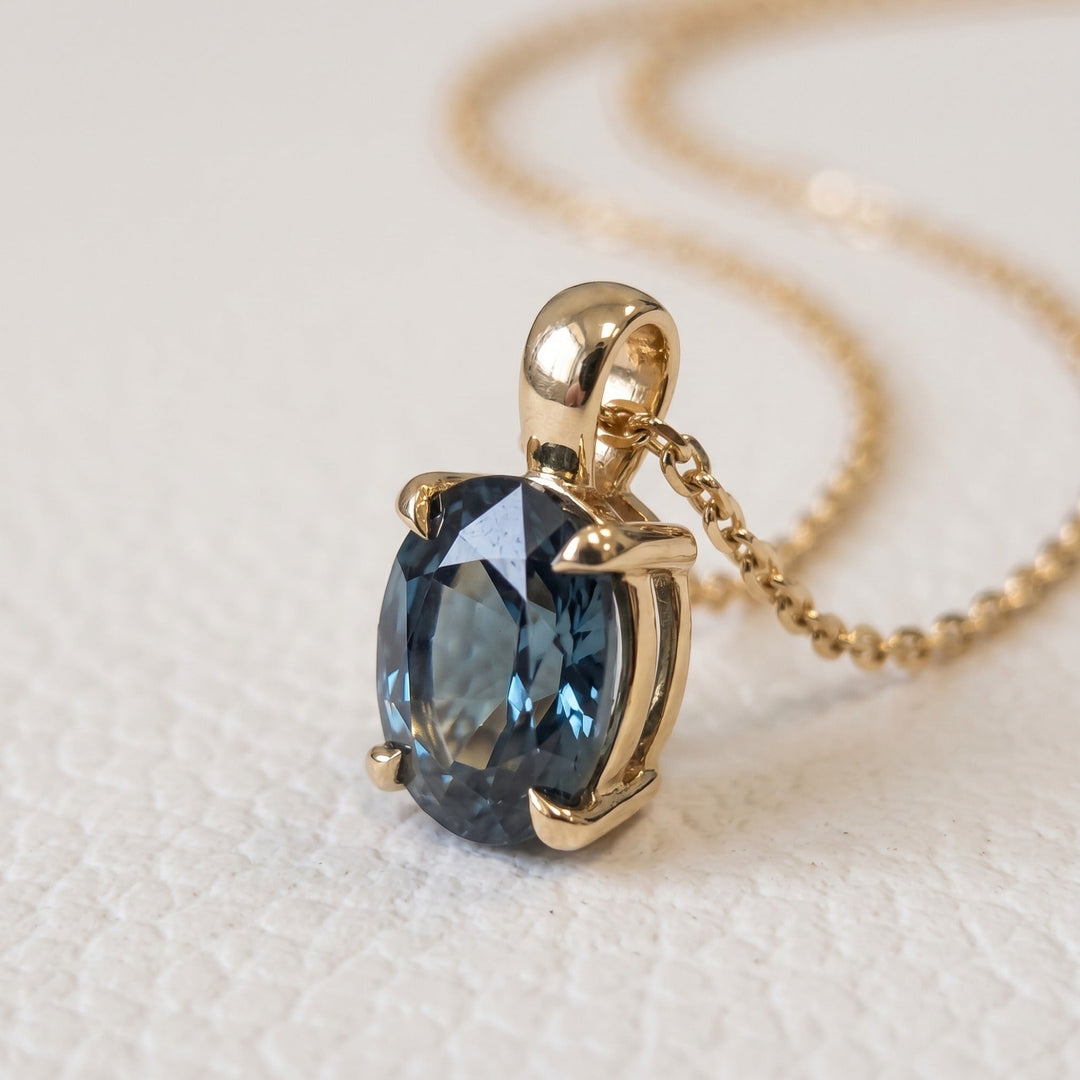 Close-up of an oval natural teal sapphire pendant in 14K yellow gold