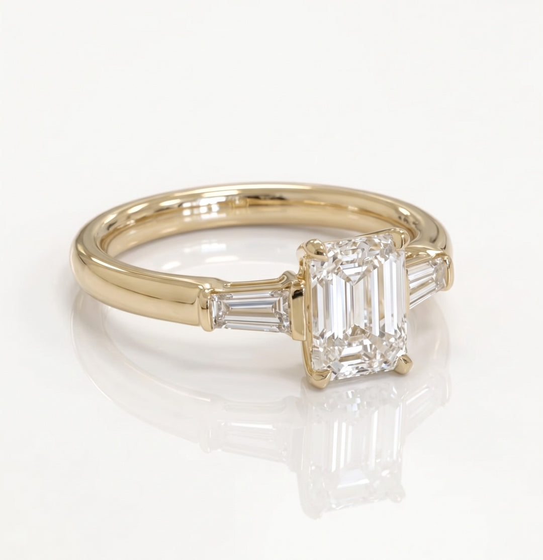 Three-quarter view of an emerald-cut and tapered-baguette natural diamond ring in yellow gold