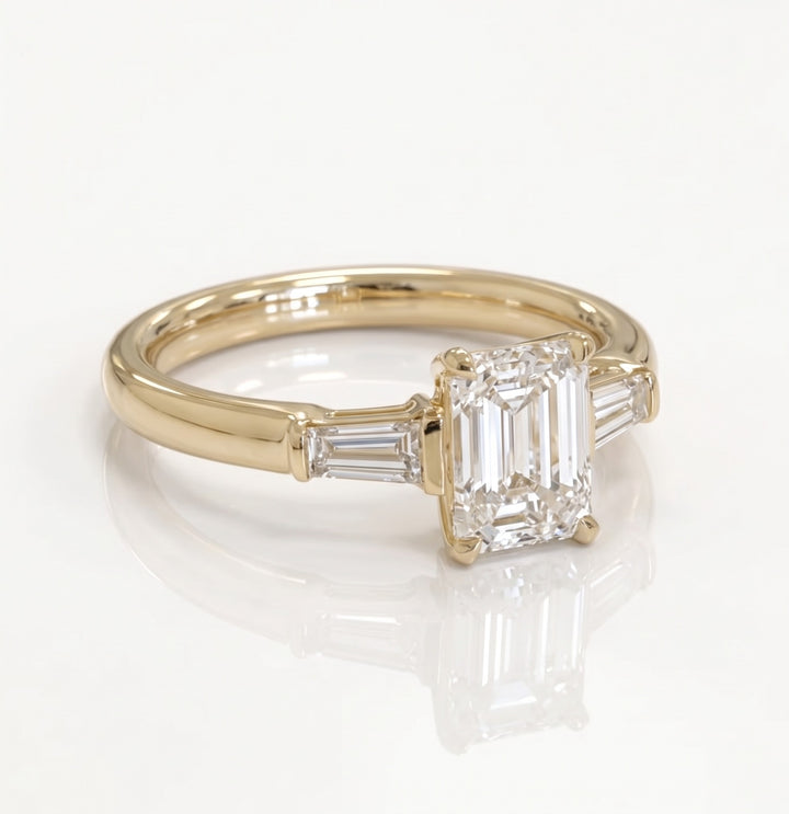 Three-quarter view of an emerald-cut and tapered-baguette natural diamond ring in yellow gold